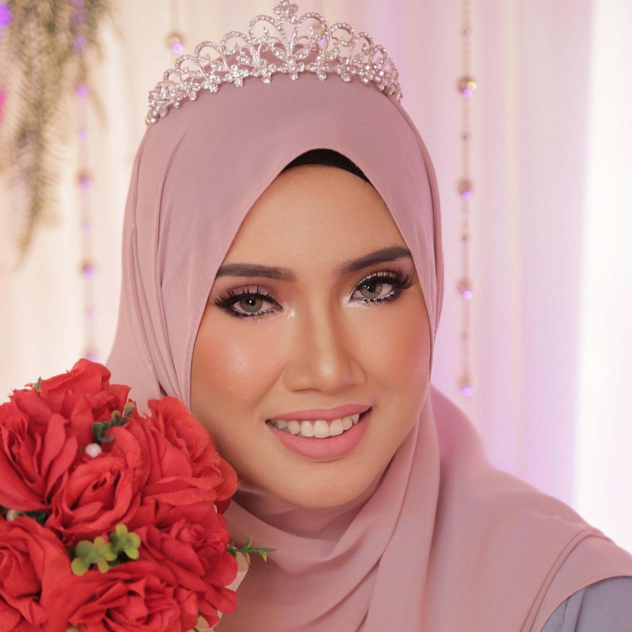 Beautiful Muslim bride portrait in pink hijab holding a red rose bouquet.